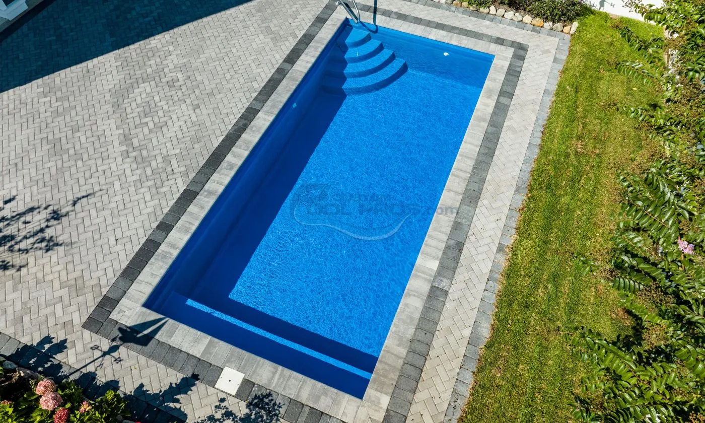 Aerial view of a modern rectangular swimming pool with clear blue water, surrounded by gray stone paving and a well-maintained green lawn. Ideal for outdoor relaxation and recreation, luxury pool builder.