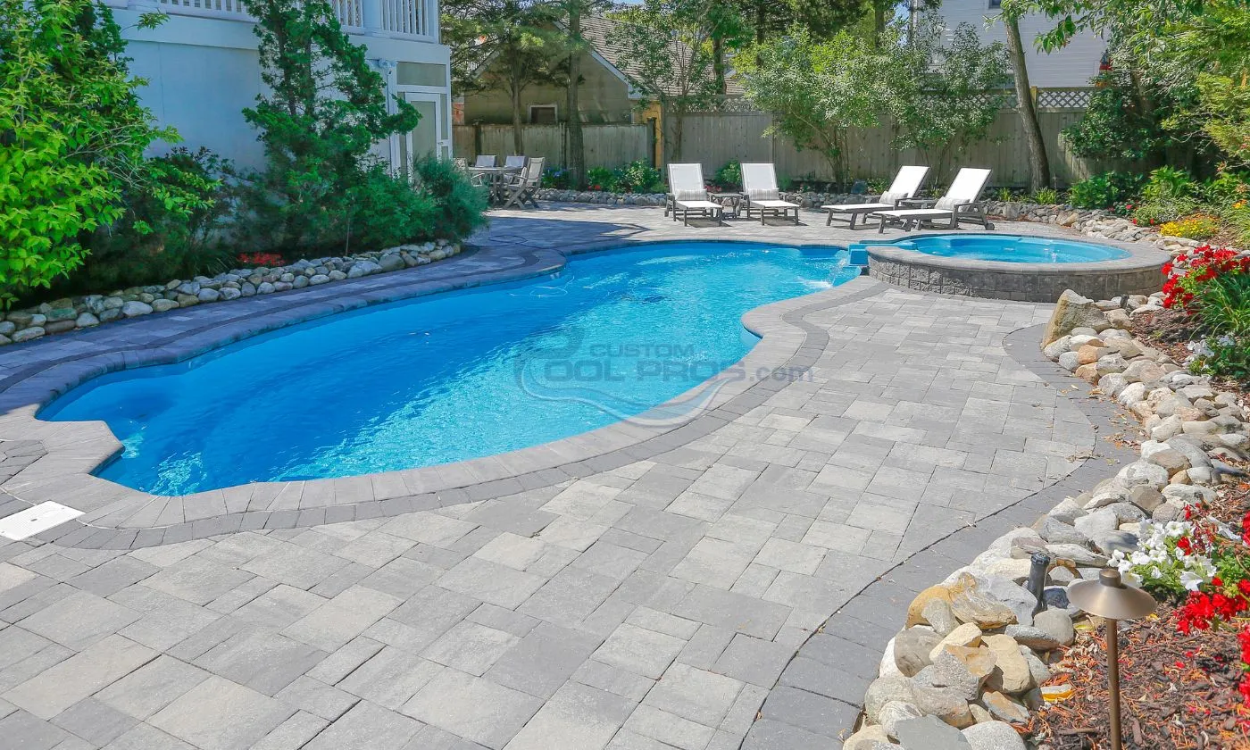 Luxury backyard pool with a curved shape, surrounded by stone pavers and lounge chairs, set in a landscaped garden. Perfect for relaxation and outdoor entertaining, swimming pool construction nj