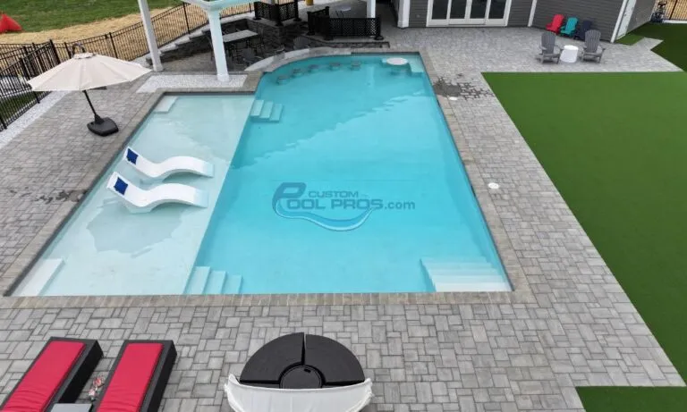 Aerial view of a modern swimming pool with a spa area, surrounded by stone pavers and a green lawn, highlighting the clear blue water and elegant design, pool installation